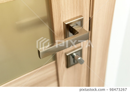 Modern chrome metal door handle on wooden door. 98473267