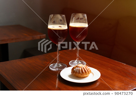 Nitro cold brew coffee drink with ice in coffee shop cafe, alternative coffee, v60. Two glasses with a soft drink and a profiterole dessert on the table. 98473270