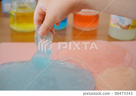 用有色水製作黏液。一名小學生正在用手拉伸黏液。 98473343