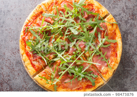 Classic Italian Pizza Prosciutto with tomato sauce, mozzarella, ham, arugula close-up on a wooden board. Horizontal top view 98473876