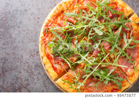 Pizza Prosciutto cooked with tomato sauce, mozzarella, ham, arugula, parmesan close-up on a wooden board. Horizontal top view 98473877