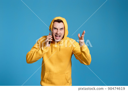 angry man in yellow sweatshirt holding mobile phone 98474619