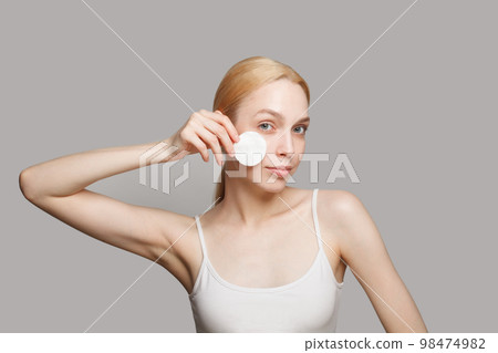 Pretty woman cleaning her face with a lotion and a cotton pad, closeup portrait 98474982