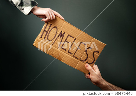 A woman and a man hold a cardboard sign with the inscription HOMELESS. Dark background. Hands close-up. The concept of helping vagabonds and panhandle A woman and a man hold a cardboard sign with the inscription HOMELESS. Dark background. Hands close-up. The concept of helping vagabonds and panhandle 98475443