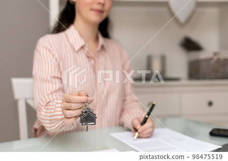 Realtor woman shows keys and writes documents. Close-up of hand. Concept of leasing and mortgage Realtor woman shows keys and writes documents. Close-up of hand. Concept of leasing and mortgage 98475519