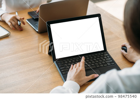 Working woman. Computer mockup. Office routine. Unrecognizable lady typing laptop blank screen sitting desk with female colleague in light room interior. 98475540