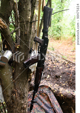 An automatic rifle near a tent in the forest, a military tent in the forest during the war in Ukraine. An automatic rifle near a tent in the forest, a military tent in the forest during the war in Ukraine. 98475814