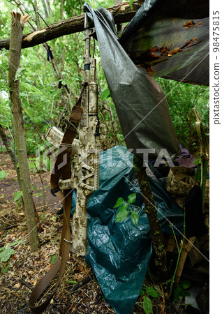 An automatic rifle near a tent in the forest, a military tent in the forest during the war in Ukraine. An automatic rifle near a tent in the forest, a military tent in the forest during the war in Ukraine. 98475815