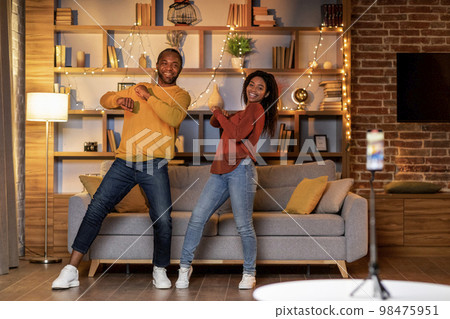 Couple recording video content, dancing on smartphone camera at home 98475951