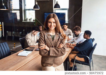 Happy caucasian businesswoman posing standing with folded arms in modern office during corporate meeting Happy caucasian businesswoman posing standing with folded arms in modern office during corporate meeting 98475972