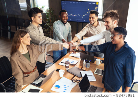 Support and teamwork concept. Young multicultural group of business people making fist bump above desk in office Support and teamwork concept. Young multicultural group of business people making fist bump above desk in office 98475981