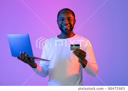 Happy african american man holding laptop and credit card Happy african american man holding laptop and credit card 98475983