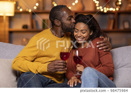 Cheers. Closeup of beautiful smiling young american couple drinking red wine, holding glasses and toasting, having romantic dinner, spending time together. Young black family celebrating Cheers. Closeup of beautiful smiling young american couple drinking red wine, holding glasses and toasting, having romantic dinner, spending time together. Young black family celebrating 98475984
