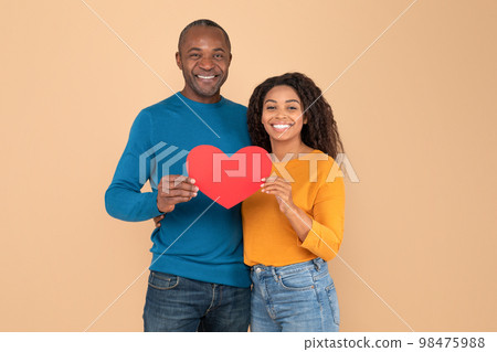 Loving african american couple holding big red heart shaped card together, celebrating St Valentine's Day Loving african american couple holding big red heart shaped card together, celebrating St Valentine's Day 98475988