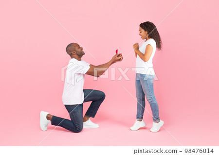Loving black middle aged man standing on one knee and offering engagement ring to his beloved young woman Loving black middle aged man standing on one knee and offering engagement ring to his beloved young woman 98476014