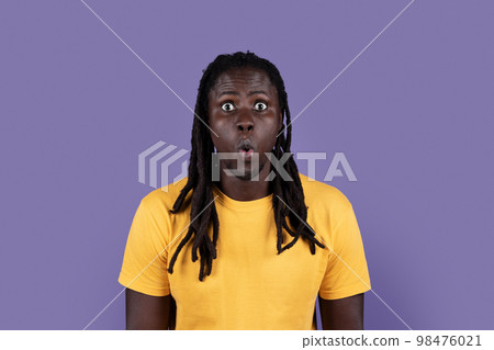Portrait of astonished black guy posing on purple 98476021