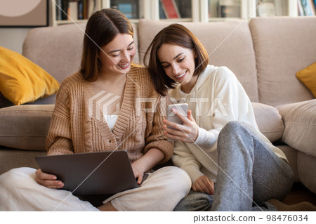 Smiling european young women with laptop and smartphone surfing in internet, chatting, show video Smiling european young women with laptop and smartphone surfing in internet, chatting, show video 98476034