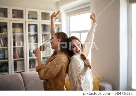 Happy excited european young superstar ladies have fun, sing song at imaginary microphone, enjoy free time Happy excited european young superstar ladies have fun, sing song at imaginary microphone, enjoy free time 98476183