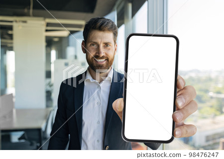 Happy middle aged businessman showing smartphone with white screen at office, mockup for mobile app or website design 98476247