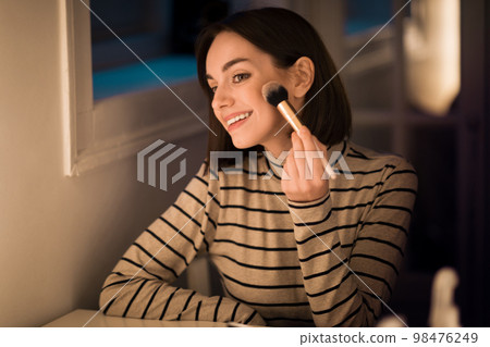 Beautiful young woman applying blush with brush Beautiful young woman applying blush with brush 98476249