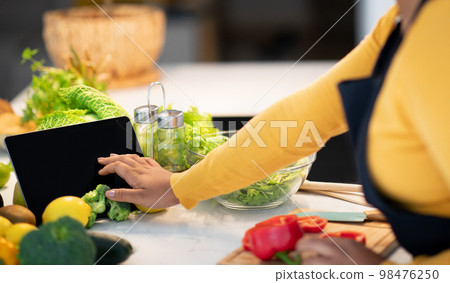 Young african american lady cook in apron use tablet with blank screen, watch food blog at table 98476250