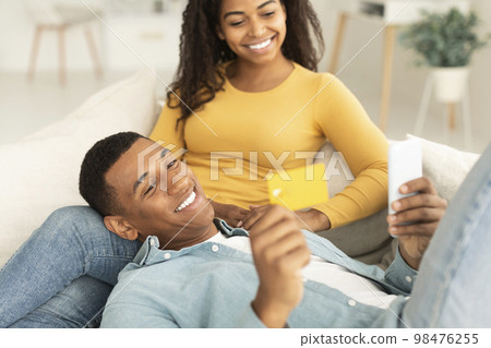Happy young african american guy show smartphone and credit card to lady, shopping online together 98476255