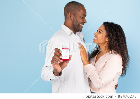 Affectionate black couple hugging and looking at each other, middle aged man holding box with engagement ring Affectionate black couple hugging and looking at each other, middle aged man holding box with engagement ring 98476275