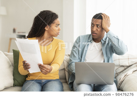 Angry sad young african american female with documents scolds at guy with laptop due mistake Angry sad young african american female with documents scolds at guy with laptop due mistake 98476276