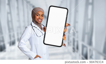 Black Muslim Doctor Lady Wearing Uniform Showing Big Blank Smartphone At Camera Black Muslim Doctor Lady Wearing Uniform Showing Big Blank Smartphone At Camera 98476314