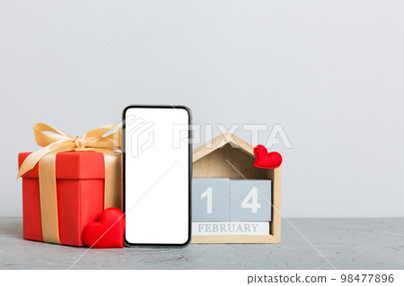 mobile phone with blank screen on colored background with hearts, calendar and gift box, valentine day 14 february concept perspertive view flat lay 98477896