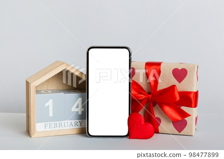 mobile phone with blank screen on colored background with hearts, calendar and gift box, valentine day 14 february concept perspertive view flat lay 98477899