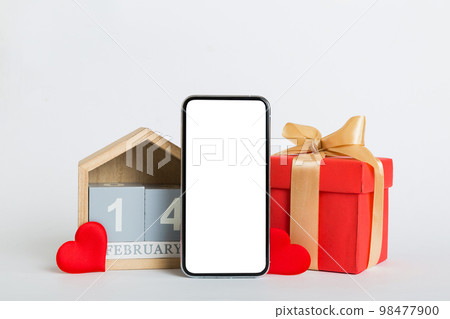 mobile phone with blank screen on colored background with hearts, calendar and gift box, valentine day 14 february concept perspertive view flat lay 98477900