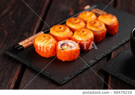 Sushi roll with salmon, avocado and tobiko caviar served on black board close-up - Japanese asian food Sushi roll with salmon, avocado and tobiko caviar served on black board close-up - Japanese asian food 98479259
