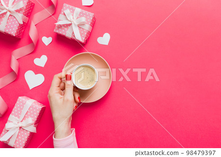 Flat lay of heart shaped cup of black coffee in the hands of women on colored background with copy space top view. Valentine day and holiday concept 98479397