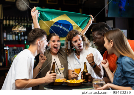 Happy friends of different ages drinking beer and celebrating the victory of the Brazilian team in night bar 98483289