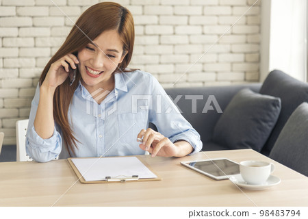 Asian women talk via smartphone work from home small office desk. Young asian Woman hands holding phone technology lifestyle. Happy Women person calling use digital smart phone working home office 98483794
