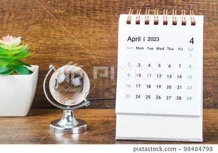 The April 2023 desk calendar for 2023 year with a crystal globe against a wooden table background. 98484798