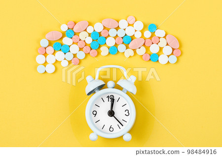 The alarm clock and many drug on a yellow background. Taking medicine at the right time concepts. The alarm clock and many drug on a yellow background. Taking medicine at the right time concepts. 98484916