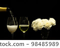 Festive party concept, Pour champagne from bottle into glass with peony in vase on black background 98485989