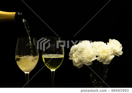 Festive party concept, Pour champagne from bottle into glass with peony in vase on black background Festive party concept, Pour champagne from bottle into glass with peony in vase on black background 98485993
