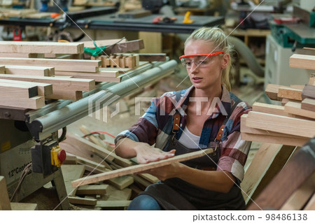 young carpenter woman wear uniform and goggles choose the size and quality wood used for work. young carpenter woman wear uniform and goggles choose the size and quality wood used for work. 98486138