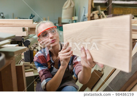 young carpenter woman wear uniform and goggles choose the size and quality wood used for work. 98486159