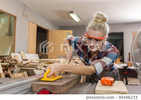 young carpenter woman wear uniform and goggles working use electronic saw cutting wood. 98486233
