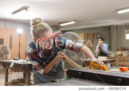 young carpenter woman wear uniform and goggles working use electronic saw cutting wood 98486234