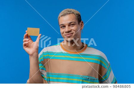 Successful handsome man showing unlimited gold credit card and look to camera blue studio background 98486805