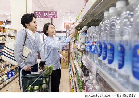 一對夫婦帶著帶智能手機收銀機的手推車購物 98486818