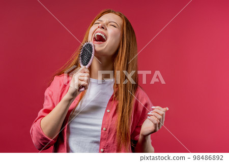 Woman singing, dancing with hair brush instead microphone on pink background. Lady having fun Woman singing, dancing with hair brush instead microphone on pink background. Lady having fun 98486892