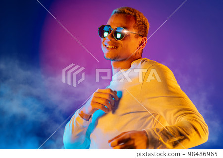 Energetic african american man dancing on colorful background under neon light. Portrait of stylish 98486965
