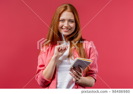 Young woman writing notes in planner with pen. Ginger girl thinking about future plans and to-do Young woman writing notes in planner with pen. Ginger girl thinking about future plans and to-do 98486980