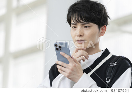 Young man thinking while looking at smartphone screen 98487964